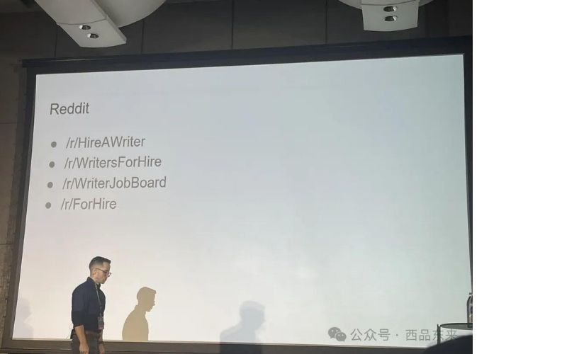 一个人在演讲台上展示幻灯片，幻灯片上列出了Reddit相关的几个子版块：/r/HireAWriter、/r/WritersForHire、/r/WriterJobBoard、/r/ForHire。