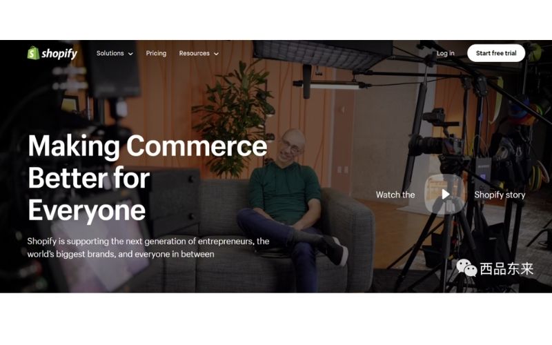 商店页面上方是Shopify的品牌标识,页面中心显示宣传语“Making Commerce Better for Everyone”,背景是一位坐在沙发上的人,周围有摄影设备。