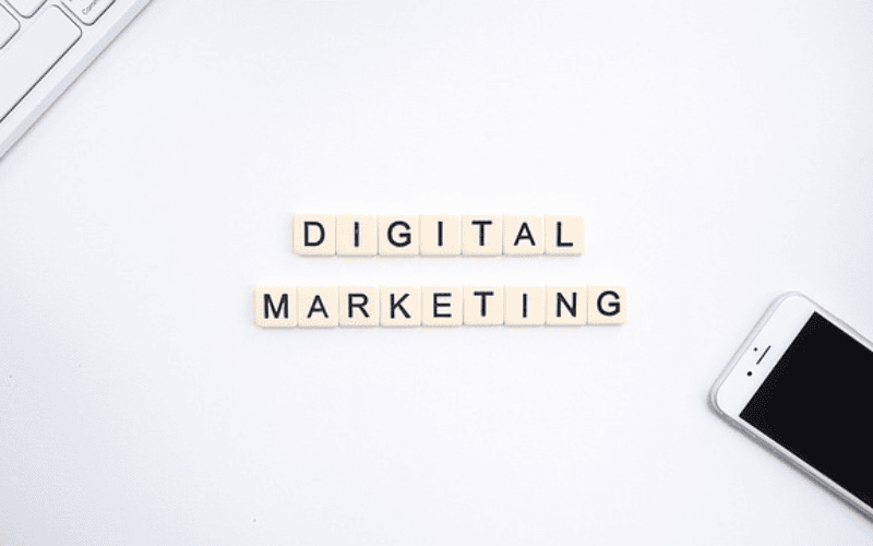 白色背景上的数字营销概念图,拼字方块拼出 DIGITAL MARKETING,旁边有键盘和手机
